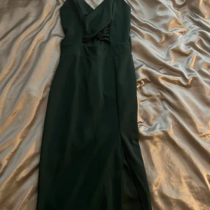 Mörk Grön klänning med slits  - Elegant mörk grön långklänning med en stilren design och en smickrande slits. Klänningen har en v-ringad hals och är ärmlös, Den har justerbara ban och har endast använts 1 gång och är i nyskick!