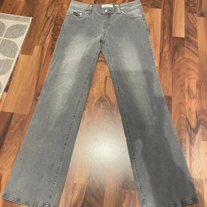 Grå jeansbyxor från John Baner - Lägre midja. Snygga grå jeansbyxor från John Baner med broderade detaljer på bakfickorna. Byxorna har en klassisk femficksdesign och en knappgylf. Perfekta för en avslappnad stil med en touch av unik design.