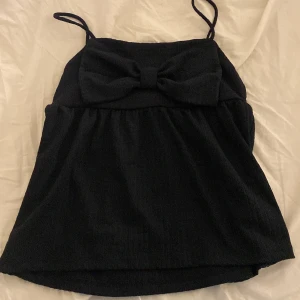 Mörkblå topp med rosett - Snygg mörkblå topp med en stor rosett framtill. Använd en gång för den blev för kall att använda. Alltså inga defekter alls. Har smala axelband och en väldigt lätt rynkad design, väldigt fint och somrigt 💕 pris kan diskuteras 