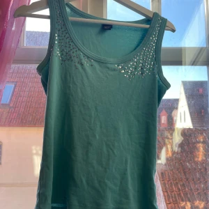 Grön topp från Esprit - Snygg linnetopp från Esprit med glittriga detaljer vid halsringningen. Perfekt för att lägga till lite bling i vardagen. Tillverkad i mjukt material för en bekväm passform. Hög rygg och låg vid bröstet. Paljetter på sidorna och tjocka band.