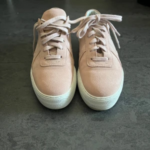 rosa sneakers från Axel Arigato - Snygga rosa sneakers från Axel Arigato i mocka med snörning. Perfekta för en stilren look. Skorna har en vit sula som ger en fräsch kontrast till den mjuka mockan. Använda två gånger så gott som nya. Vid fler frågor, hör gärna av er! 