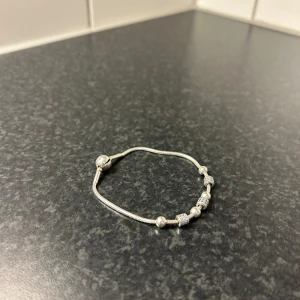 Silverfärgat armband med berlocker - Elegant silverfärgat Pandora armband med flera dekorativa berlocker. Armbandet har en stilren design med små detaljer som ger det en unik touch. Perfekt för att komplettera din look med en subtil glans.