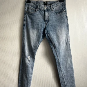 Blå super skinny jeans från H&M - Snygga ljusblå super skinny jeans från H&M med slitna detaljer på benen. Perfekta för en trendig look. De har en klassisk femficksdesign och knappgylf.