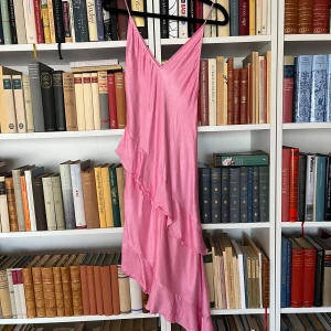 Rosa klänning med volanger - Säljer en söt rosa klänning i satin med volanger och smala axelband. Klänningen har en v-ringad design och är perfekt för sommaren eller fest.🩷Använd och rvättad en gång