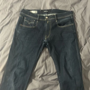 Mörkblå jeans från Replay - Snygga mörkblå jeans från Replay Anbass med klassisk femficksdesign och kontrasterande sömmar. De har en dragkedja och knapp framtill samt stilrena bakfickor med dekorativa sömmar. Perfekta för en avslappnad look.