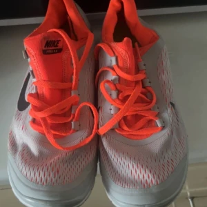 Nike Free 5.0 löparskor - Säljer ett par Nike Free  löparskor i vitt med orange detaljer och snörning.