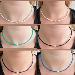 Färgglada halsband och armband med pärlor - Säljer ett set med färgglada halsband och matchande armband, alla med en central pärla. Halsbanden och armbanden finns i färgerna vit, svart, turkos, blå, rosa och lila. Perfekt för att lägga till en färgklick i din outfit.