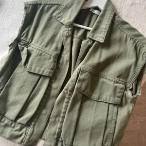 Olivgrön väst från Zara - Säljer en stilren olivgrön väst från Zara med knappar framtill och två stora fickor på bröstet. Perfekt för lager-på-lager-stil och ger en cool touch till din outfit.