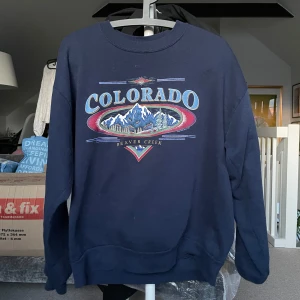 Mörkblå sweatshirt med Colorado-tryck - Säljer en mörkblå sweatshirt med ett stort tryck av Colorado och Beaver Creek i mitten. Tröjan har långa ärmar och en rund halsringning. Är i storlek L, men är liten i storlek.