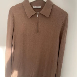 Half-zip från Tiger Of Sweden - Snygg beige tröja från Tiger of Sweden med dragkedja vid halsen. Tröjan har en klassisk krage och långa ärmar, perfekt för en stilren look. Passar bra till både vardag och mer uppklädda tillfällen. Storlek S. Nypris 1400kr