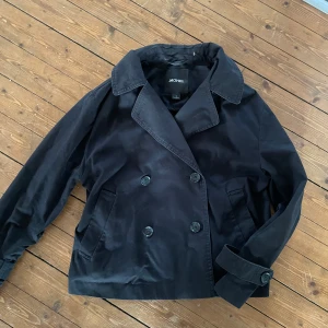 Svart trenchcoat från Monki - Snygg svart kappa från Monki med dubbelknäppning och klassisk krage. Använd max 5 gånger, nästan helt ny förutom en oboy fläck som knappt syns som säker kan tas bort lätt med rätt medel. Storlek S
