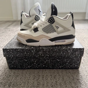 Nike Air Jordans i vit och svart - Snygga Nike Air Jordans i vit och svart med detaljer i mocka. Skorna har en klassisk design med snörning och en robust sula. Perfekta för dig som vill ha en stilren look med en sportig touch.