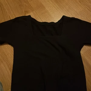 Svart topp med fyrkantig urringning - Säljer en stilren svart topp med fyrkantig urringning. Perfekt för en minimalistisk look. Toppen har korta ärmar och är gjord i ett mjukt material.