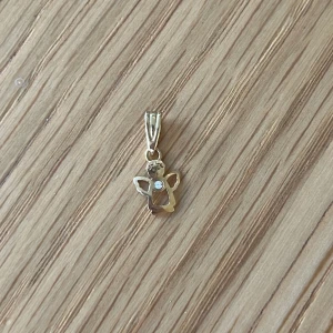 Berlock i guld med vit sten - Ängel-berlock i guld med en vit sten. Passar till att hänga på halsband. Märket är okänt.