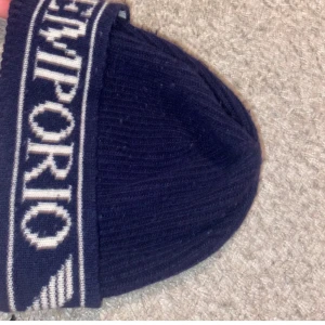 Äkta mössa från Emporio Armani - Snygg mörkblå mössa från Emporio Armani med ribbad design och märkets logga i kontrasterande färg. Perfekt för att hålla värmen med stil.