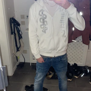 Vit hoodie från Zantiore - Säljer en vit hoodie från Zantiore med dragkedja och ett coolt ormmönster på framsidan. Hoodien har en bekväm passform och är perfekt för en avslappnad stil. Den har också en praktisk huva och fickor framtill. Storlek M men passar även S. Aldrig använd ute bara inomhus när man chillar.