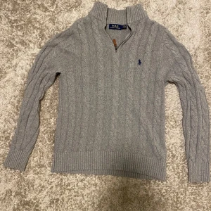 Grå stickad tröja från Polo Ralph Lauren - Tja, Säljer en stilren grå stickad tröja från Polo Ralph Lauren med dragkedja och ribbad krage, den är i  storlek m. Den är i jättebra skick, Tröjan har ett diskret kabelstickat mönster och långa ärmar. Perfekt för kyliga dagar. Den går för runt 2700 kr i butik, men jag säljer den för 1849 kr.Priset kan diskuteras vid snabb affär! 🙌🔥