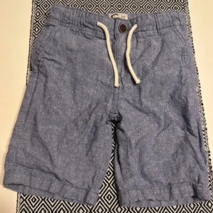 Blå shorts med snörning - Snygga blå shorts med snörning i midjan och knappdetalj. Perfekta för en avslappnad sommarstil.