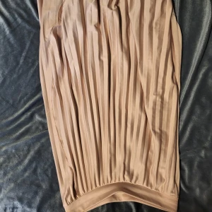 Beige plisserad kjol från Reserved - Elegant beige plisserad kjol från Reserved. Kjolen har en mjuk och flödande design med elastisk midja för bekväm passform. Perfekt för en stilren look.