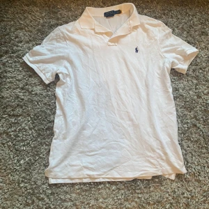 Vit pikétröja från Ralph Lauren - Säljer en klassisk vit pikétröja från Ralph Lauren med broderad logga i marinblått på bröstet. Tröjan har korta ärmar och en stilren krage med knappar. Perfekt för en avslappnad och stilren look. Pris ej hugget i sten