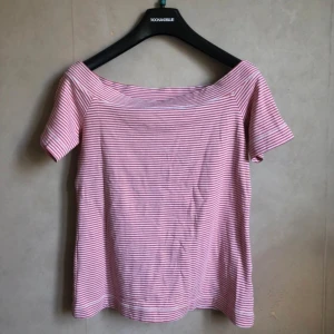 Randig offshoulder topp - Säljer en söt randig offshoulder topp i rosa och vit. Toppen har korta ärmar och en bekväm passform, perfekt för sommardagar. Den är gjord i ett mjukt material som känns skönt mot huden.