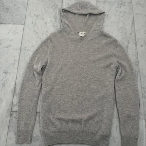 Grå kashmir hoodie från Soft Goat - Säljer en supermjuk grå hoodie i 100% kashmir från Soft Goat. Tröjan har långa ärmar och stilrena armbågslappar i en mörkare nyans. Perfekt för kyliga dagar när du vill vara både bekväm och snygg. Kommer i original kartong.