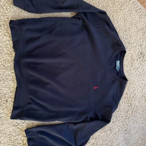 Mörkblå tröja från Polo Ralph Lauren - Säljer en stilren mörkblå tröja från Polo Ralph Lauren med det klassiska röda logotypbroderiet på bröstet. Tröjan har långa ärmar och en rund halsringning. Perfekt för en avslappnad och snygg look.