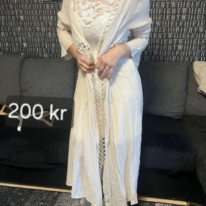 Vit spetsklänning med lång kappa - Elegant vit spetsklänning med en matchande lång kappa. Klänningen är ärmlös och kort, medan kappan har långa ärmar och dekorativa spetsdetaljer. Perfekt för en stilfull look. Lång tunika tröja Onesize och vit klänning S