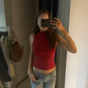 Röd ärmlös topp - Snygg röd ärmlös topp med hög hals. Perfekt för en stilren look. Passar bra till jeans eller kjol.