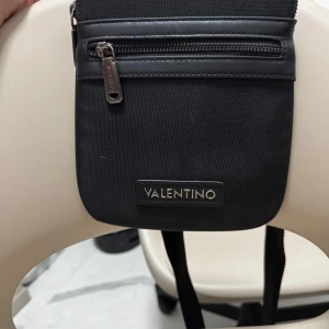 Svart axelväska från Valentino - Snygg svart axelväska från Valentino med dragkedja framtill. Perfekt för att bära med sig det viktigaste. Stilren design med en diskret logotyp i silver. Pros kan diskuteras