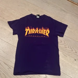 Lila T-shirt från Thrasher I storlek S  - Säljer en cool lila T-shirt från Thrasher med den ikoniska loggan i eldflammor på bröstet. Perfekt för skate-entusiaster eller streetwear-fans. T-shirten har en klassisk passform och är kortärmad.
