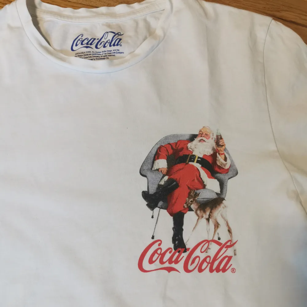 Säljer två vita t-shirts med julmotiv. Den ena från Jack & Jones har en bulldog med tomteluva och texten 'Deck Me Out'. Den andra från Coca-Cola har en bild av jultomten med Coca-Cola-loggan. Perfekta för julfirandet!. T-paidat.