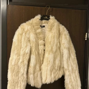 Beige pälsjacka  - Säljer en fluffig och trendig beige pälsjacka med långärmad design. Perfekt för att hålla sig varm och stilren under kyliga dagar. Jackan har en mjuk och lyxig känsla.