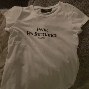 Vit t-shirt från Peak Performance - Säljer en stilren vit t-shirt från Peak Performance med tryck på framsidan. Perfekt för en avslappnad look.