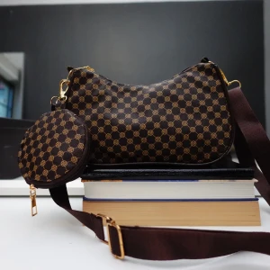 Brun mönstrad axelväska med rund plånbok - Snygg brun axelväska med ett guldmönster och matchande rund plånbok. Väskan har en justerbar axelrem och dragkedja i guld. Perfekt för att bära dina nödvändigheter med stil.