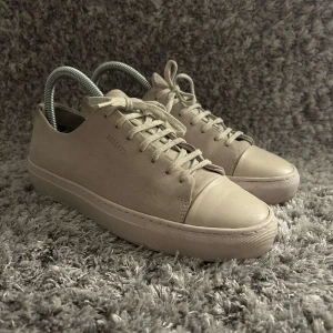 Beige sneakers från Axel Arigato - Snygga beige sneakers från Axel Arigato med stilren design. Skorna är i strl 39,5 och är använda men har kvar o ge, inget og tillkommer.