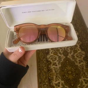 Solglasögon från Chimi - Snygga solglasögon från Chimi med rund form och transparent rosa korall båge. Glasen har en rosa ton som ger en cool look. Perfekta för soliga dagar och kommer i ett stilrent vitt fodral. Använda få gånger. 