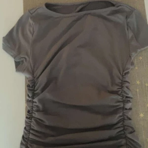 Grå kortärmad topp med rynkade sidor - Snygg grå topp med korta ärmar och rynkade detaljer på sidorna. Perfekt för en stilren look.
