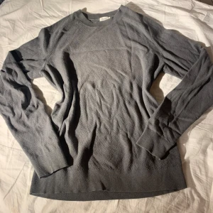 Grå stickad tröja från Filippa K - Säljer en stilren grå stickad tröja från Filippa K. Tröjan har en klassisk rund halsringning och långa ärmar, perfekt för kyligare dagar. Passar både till jeans och kjol för en avslappnad look. Inköpspris 2100kr