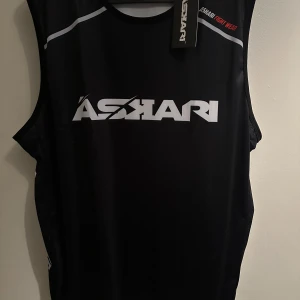 Askari Armada tank top L - Snygg svart ärmlös topp från Askari med vit logga framtill och detaljer på sidorna. Perfekt för träning eller en aktiv livsstil. Nypris 450kr aldrig använd och tagg sitter kvar 