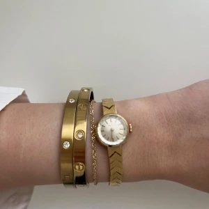 Guldfärgad klocka från Helvetia - Elegant guldfärgad vintageklocka från Helvetia med ett klassiskt armband i pilmönster. Klockan har en rund urtavla med guldmarkeringar och en subtil vit bakgrund. Behöver dock ett nytt batteri.