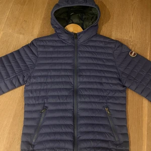 Blå dunjacka med huva - Snygg blå dunjacka från Colmar med huva och dragkedja framtill. Jackan har en quiltad design och två praktiska fickor med dragkedjor. Perfekt för kyligare dagar. Skicket är 10/10 knappt använd. Nypris är 2699, mitt pris 1000 ( kan diskuteras) hör av dig vid frågor