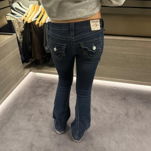 Mörkblå bootcut jeans från True Religion - Snygga mörkblå bootcut jeans från True Religion med ikoniska bakfickor. Jeansen har låg midja. Jag säljer dessa då de inte kommer till användning, jeansen är i super skick! Storlek W25