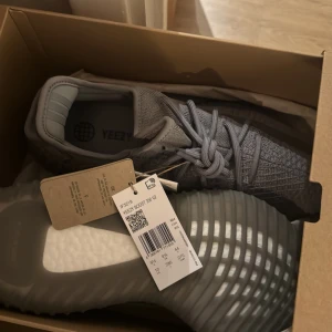 Grå Adidas Yeezy Boost 350 V2 - Säljer ett par helt nya oanvända  grå Adidas Yeezy Boost 350 V2 med stickad ovandel och snörning. Skorna har en distinkt ribbad sula och är kända för sin komfort och stil.