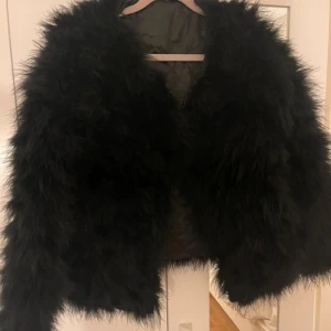 Svart pälsjacka - Snygg svart pälsjacka som ger en lyxig känsla. Perfekt för att höja din outfit till nästa nivå. Jackan har en fluffig textur och är långärmad, vilket gör den idealisk för kyligare dagar.