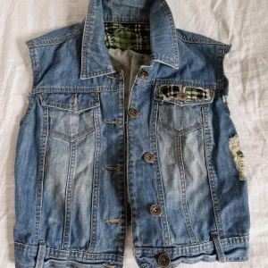 Jeansväst med grönt rutigt foder - Säljer en cool vintage jeansväst från Joe Brown's! Västen har en sliten look med flanneldetaljer och fickor framtill. 100% bomull. Uppsydd på 90-talet. Perfekt för en avslappnad eller alternativ stil :) Uppskattar till en M, mått kan fås vid intresse!