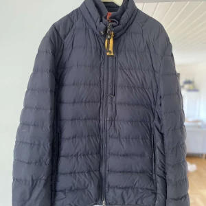 Mörkblå dunjacka från Parajumpers - Säljer en snygg och lätt mörkblå dunjacka från Parajumpers. Jackan har en quiltad design med en dragkedja framtill och en cool patch på ärmen. Perfekt för höst och vinter, den är både stilren och funktionell. Passar perfekt för dig som vill hålla värmen utan att kompromissa med stilen.