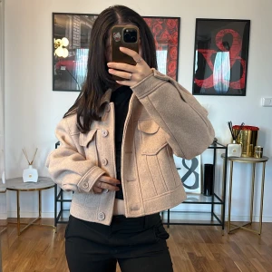 Beige jacka med knappar Na-KD - Säljer en superfin beige jacka med knappar framtill. Den har en croppad stil och stora fickor på bröstet. Perfekt för höst och vår, och den är gjord i ett mjukt material som känns som ull. Jackan har långa ärmar och en normal passform💓