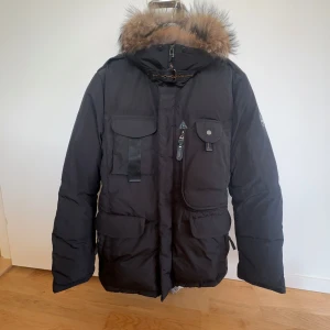 Svart vinterjacka från Hollies - Säljer en svart vinterjacka från Hollies med en mysig pälsfodrad huva. Jackan har flera praktiska fickor med både dragkedja och knappar. Perfekt för kalla vinterdagar! 🖤