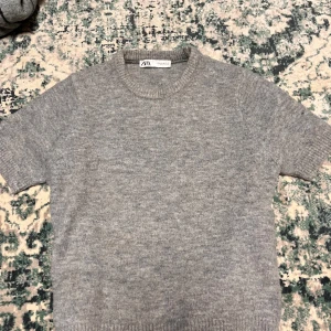 Grå tröja från Zara - Säljer en supermjuk och stilren grå tröja från Zara. Den är kortärmad och perfekt för både vardag och lite finare tillfällen. Tröjan är i ett skönt material som känns lyxigt mot huden. Passar perfekt till jeans eller kjol!